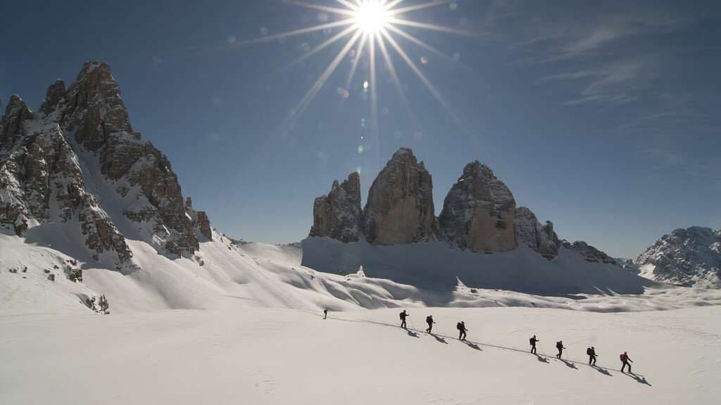 Un viaggio di gruppo WeRoad fa un'escursione in fila indiana attraverso un vasto paesaggio montano innevato sotto un cielo limpido e soleggiato.