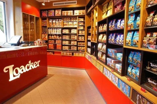 L'interno di un negozio Loacker, con un prominente bancone rosso con il logo del marchio e scaffali pieni di prodotti.