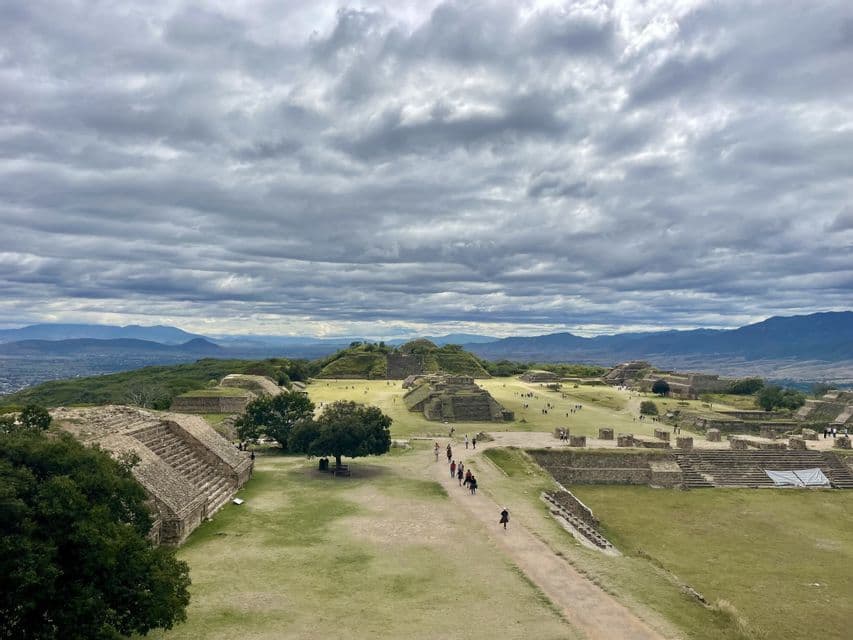 Un voyage de groupe WeRoad traverse un vaste site archéologique avec des ruines de pyramides en pierre et des pelouses vertes sous un ciel nuageux.