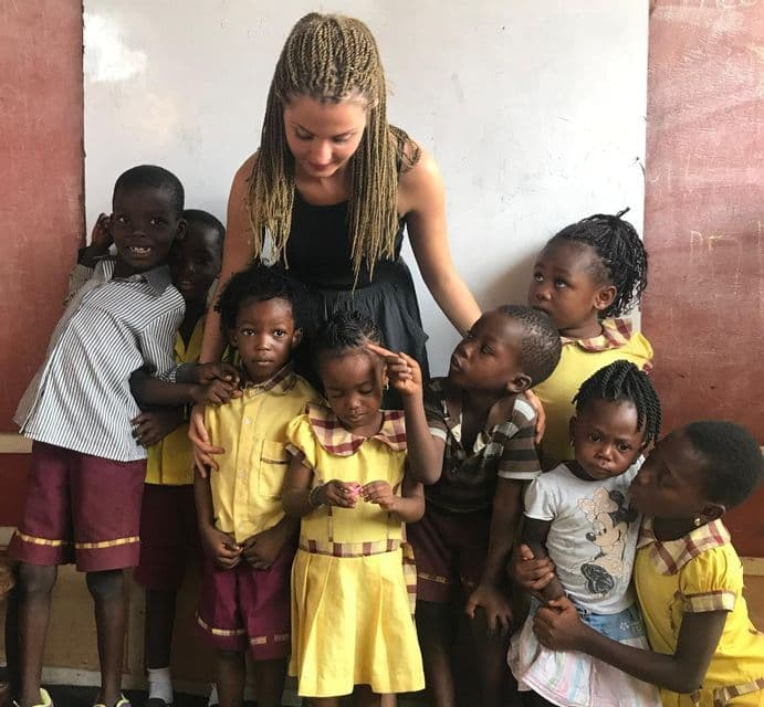 Una donna con trecce bionde si trova al centro di un gruppo di bambini in un'aula.
