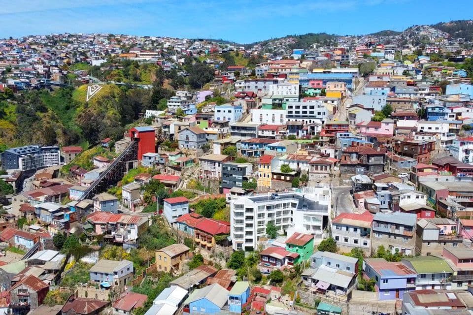 Veduta aerea di una città densamente popolata con case colorate su una collina verde, e una funicolare che ne risale il pendio.
