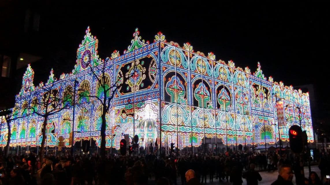 Un'elaborata facciata di un edificio, fatta di migliaia di luci colorate, illumina una grande folla durante un festival notturno.