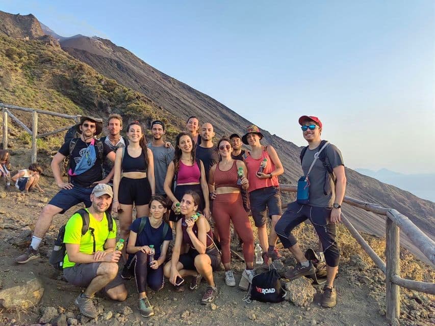 Un viaggio di gruppo WeRoad posa per una foto su un sentiero di montagna polveroso con un pendio vulcanico sullo sfondo.