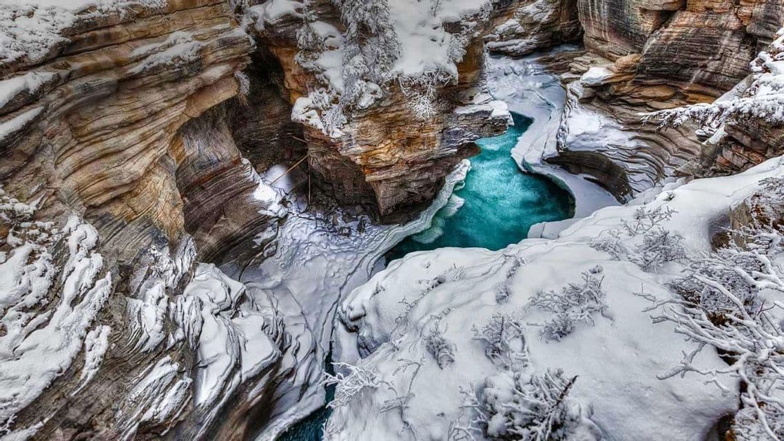 Un fiume turchese attraversa una gola stretta e innevata con pareti rocciose stratificate.