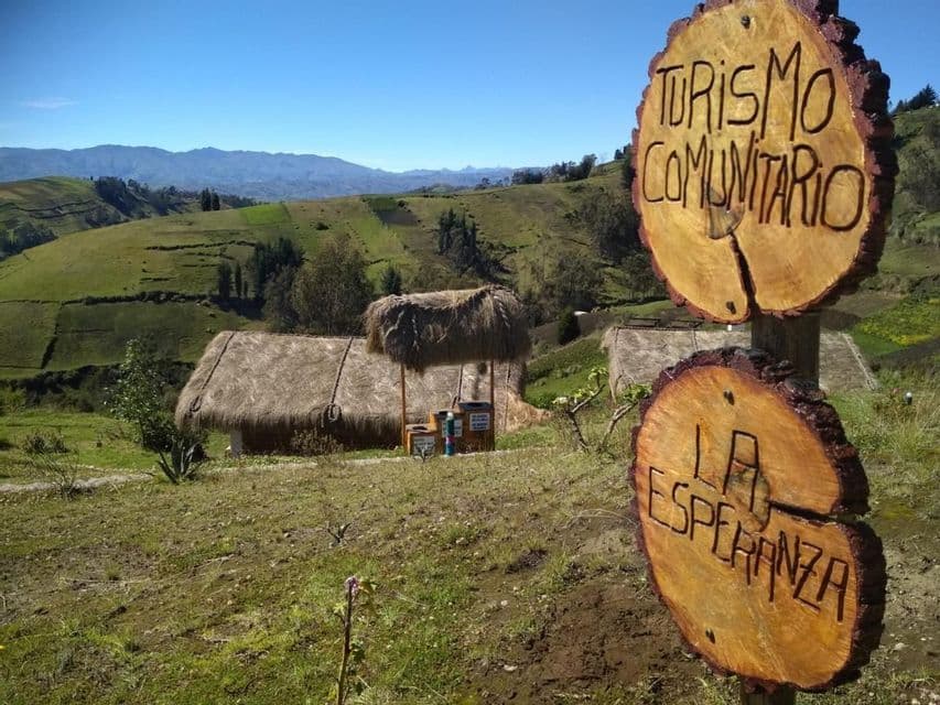 Wooden signs for 'Turismo Comunitario La Esperanza' stand in a green, hilly landscape with thatched-roof huts in the background.