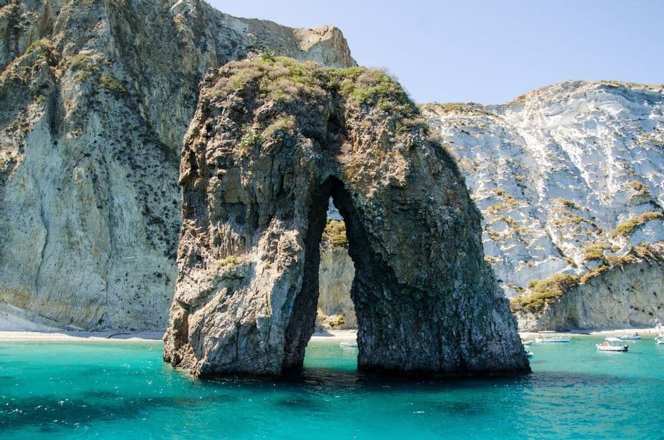 Un arco roccioso naturale si erge in acque limpide e turchesi, con una spiaggia sabbiosa e ripide scogliere alle spalle.