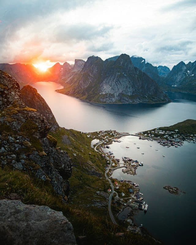 Vista aérea de un pueblo costero en un fiordo al atardecer, con montañas escarpadas surgiendo del agua.