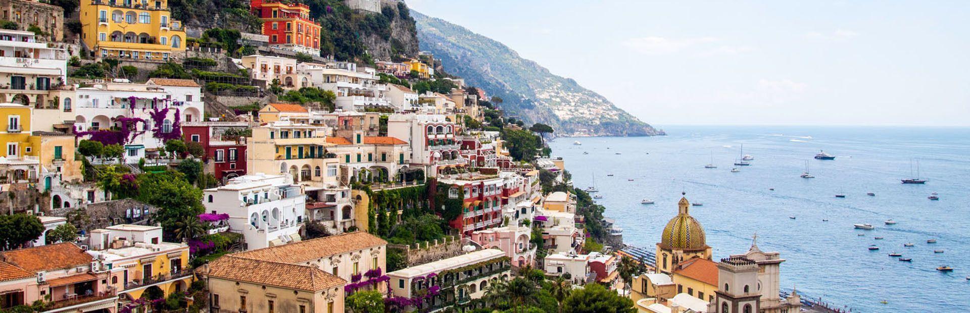 Vista panorámica de edificios coloridos en un acantilado empinado, con un mar azul salpicado de barcos bajo un cielo claro.