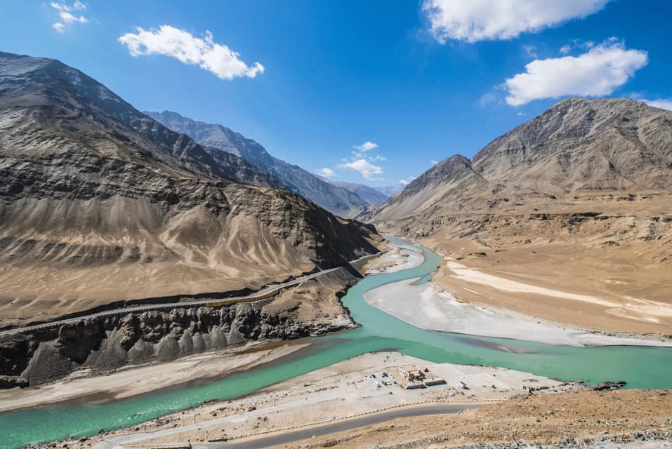 A turquoise river winds through a vast, arid valley surrounded by rocky mountains under a clear blue sky.