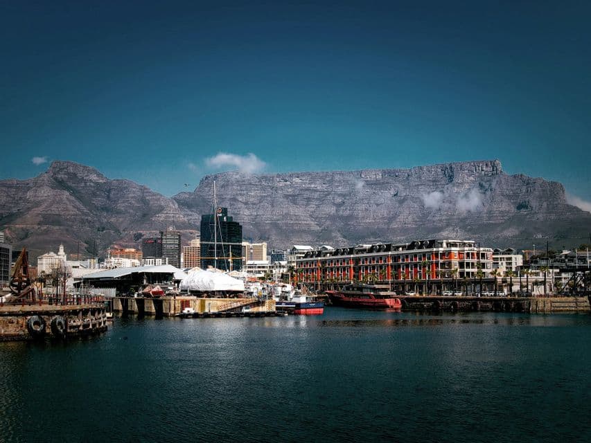 Un port urbain avec des bâtiments en front de mer, dominé par une grande montagne au sommet plat sous un ciel bleu.