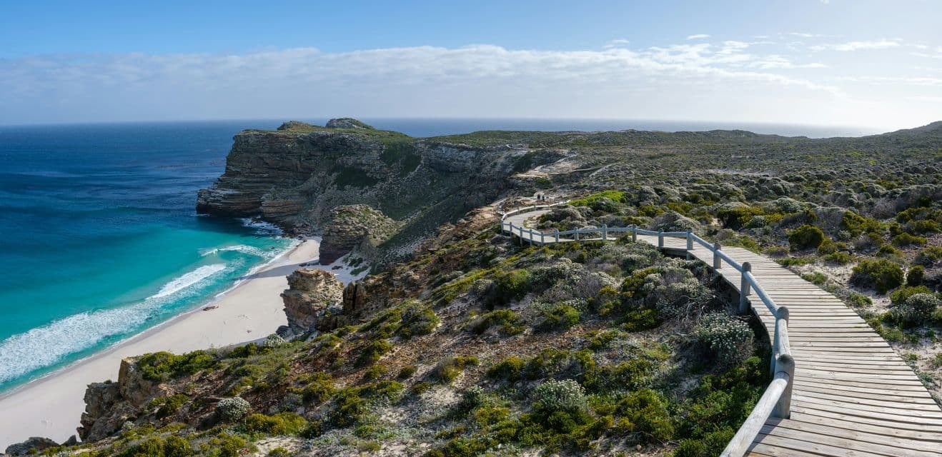Une passerelle en bois serpente le long d'une falaise escarpée, dominant une plage de sable blanc aux eaux turquoises.
