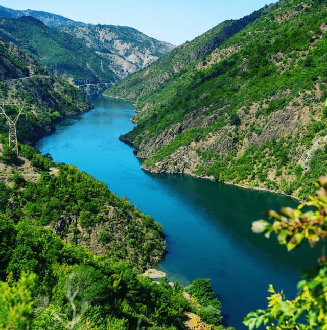 An aerial view of a wide blue river winding through a valley of steep, green mountains under a clear sky.