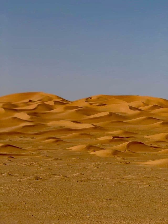 Dune di sabbia dorata nel deserto sotto un cielo limpido.