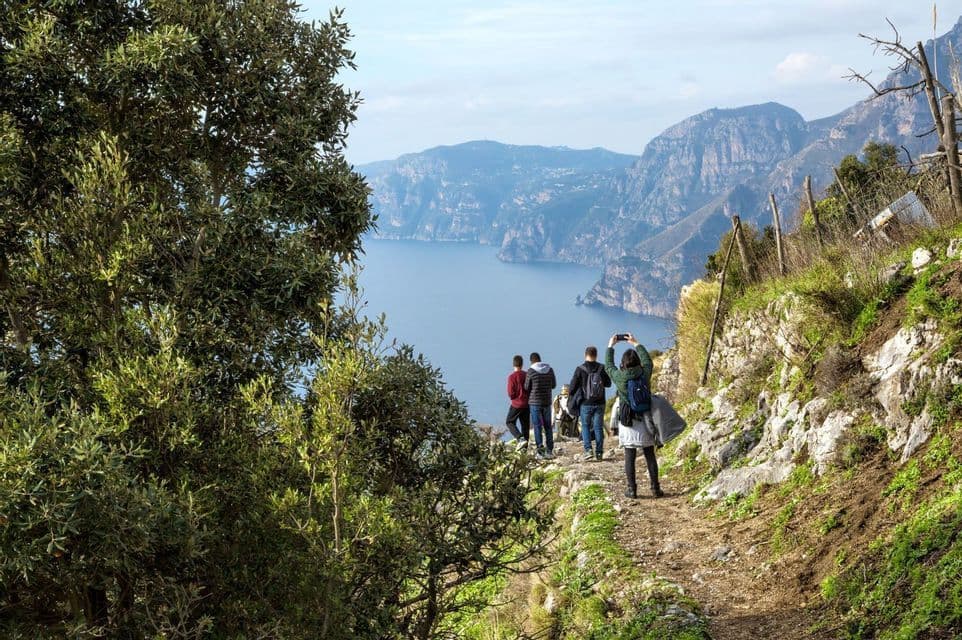 Un viaje en grupo de WeRoad recorre un sendero de montaña costero, haciendo una parada para fotografiar el inmenso mar y los acantilados.