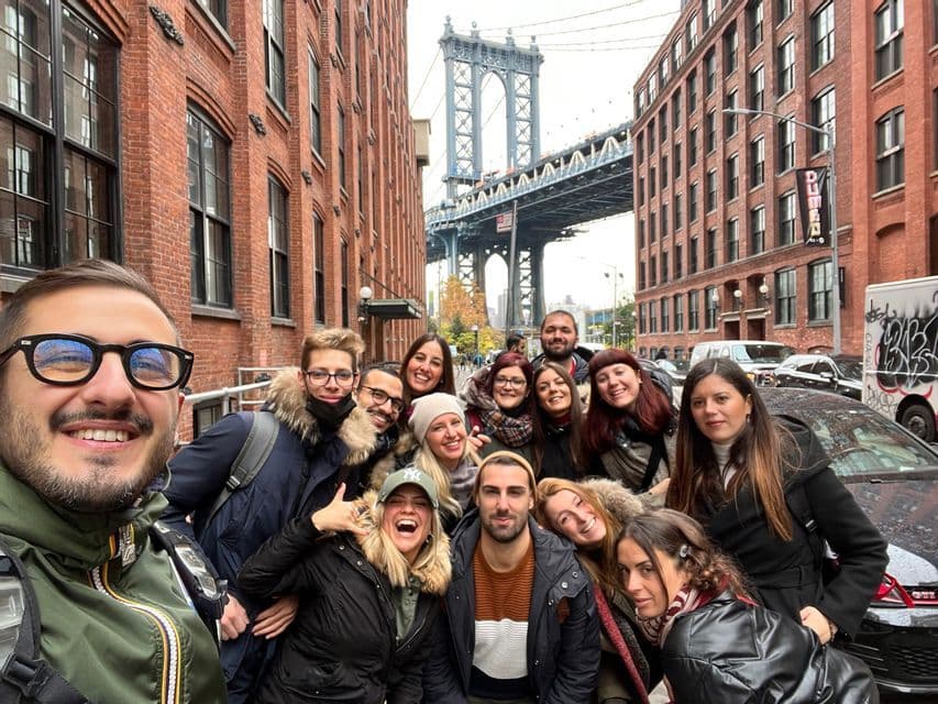 Un viaje en grupo de WeRoad tomándose una selfie grupal en una calle de la ciudad, con un gran puente visible entre edificios de ladrillo rojo.