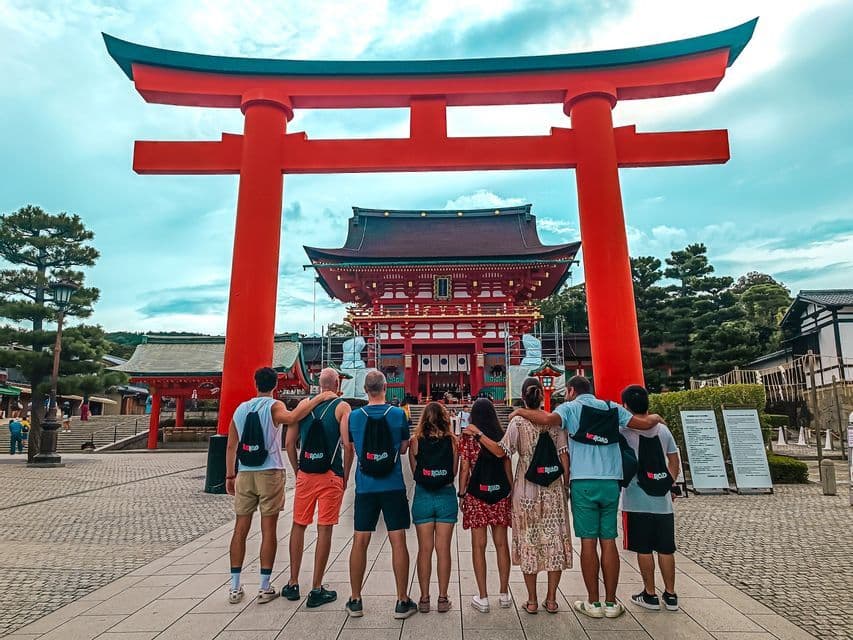 Un grupo de WeRoad de espaldas a la cámara, observando un templo japonés a través de una gran puerta torii roja.