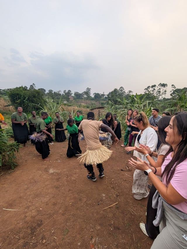 Un viaje en grupo WeRoad interactúa con artistas locales realizando una danza tradicional en círculo en un entorno rural al aire libre.