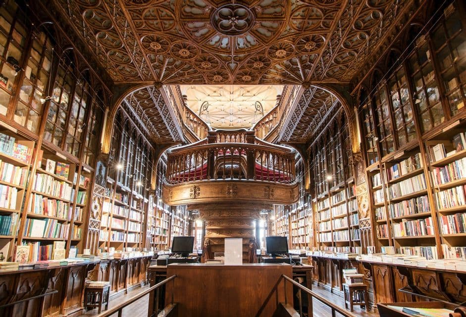 L'interno di una sfarzosa biblioteca in legno a più piani con una grande scalinata centrale e scaffali a tutta altezza.