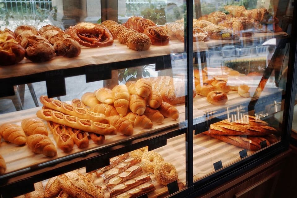 Une sélection de pains frais et de viennoiseries, incluant bretzels et croissants, présentés sur des étagères dans une vitrine de boulangerie.