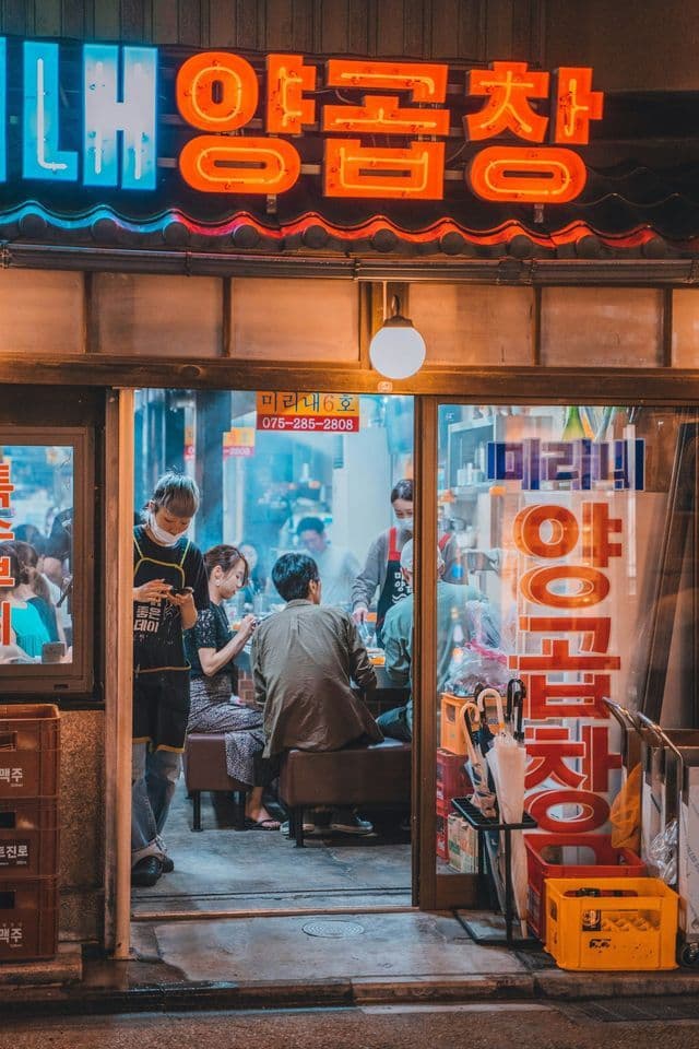 The entrance to a busy Korean restaurant at night, with people dining inside under a glowing neon sign.