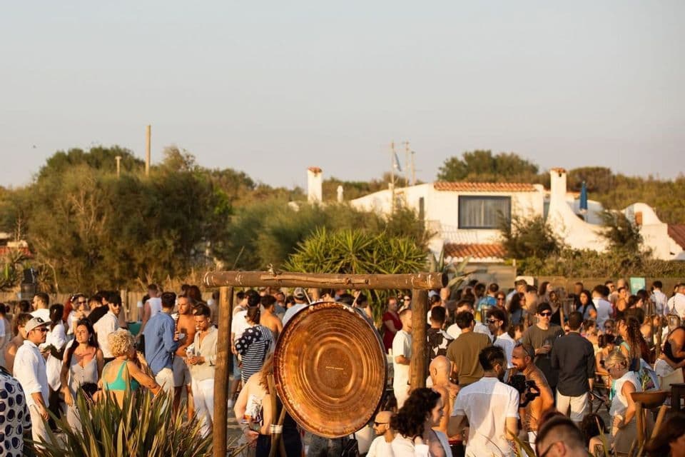 Un gruppo WeRoad si diverte a una festa in spiaggia all'aperto, con un grande gong al centro della folla.