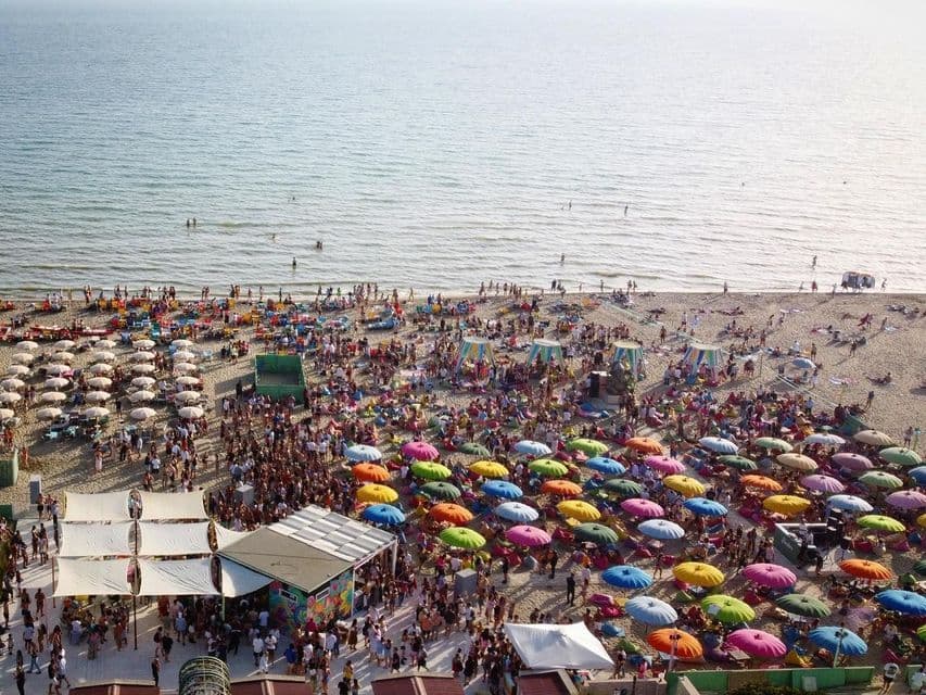 Vista aerea di una spiaggia affollata con persone e ombrelloni colorati sul mare.