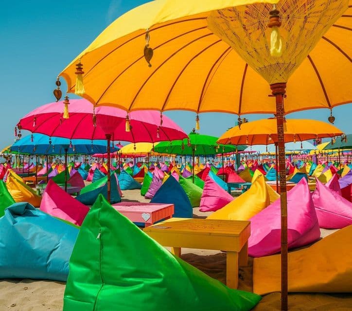 Pouf colorati e grandi ombrelloni sono allineati su una spiaggia sabbiosa sotto un cielo limpido.