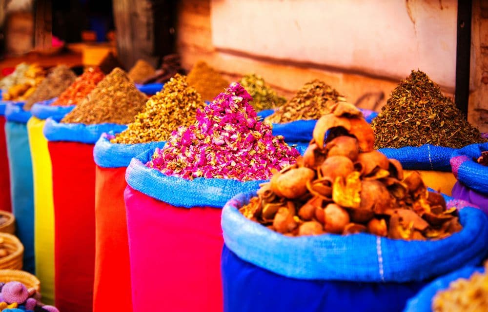 Une rangée de sacs colorés remplis de tas coniques d'épices, d'herbes et de fleurs séchées sur un étal de marché.