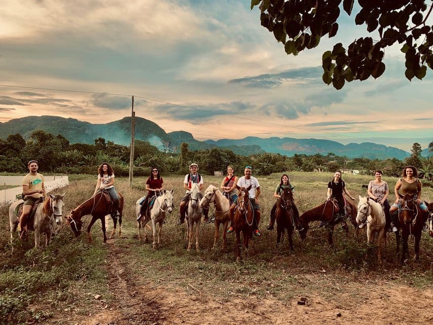 Un gruppo WeRoad in posa a cavallo in un prato verde con montagne sullo sfondo sotto un cielo nuvoloso.