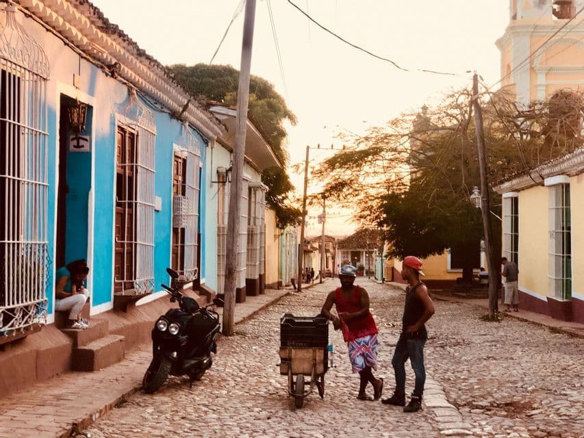 Two men talking on a cobblestone street lined with colorful colonial houses at sunset.