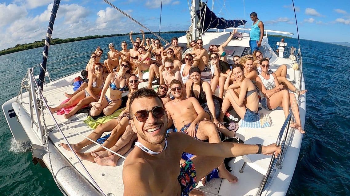 Un numeroso gruppo WeRoad sorride e posa per un selfie sul ponte di un catamarano che naviga in mare aperto.