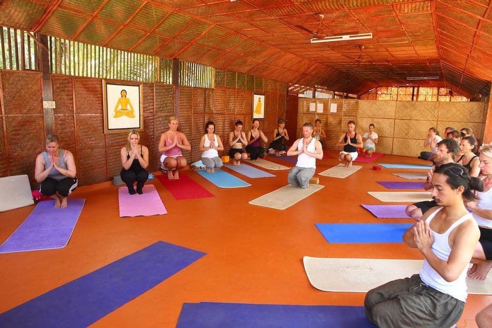 Un gruppo WeRoad partecipa a una lezione di yoga su tappetini colorati in uno studio con pavimento arancione e pareti intrecciate.
