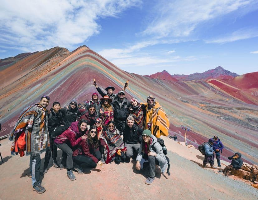 Un gruppo WeRoad posa per una foto su un fianco della montagna, con una grande montagna colorata e a strisce sullo sfondo sotto un cielo blu.