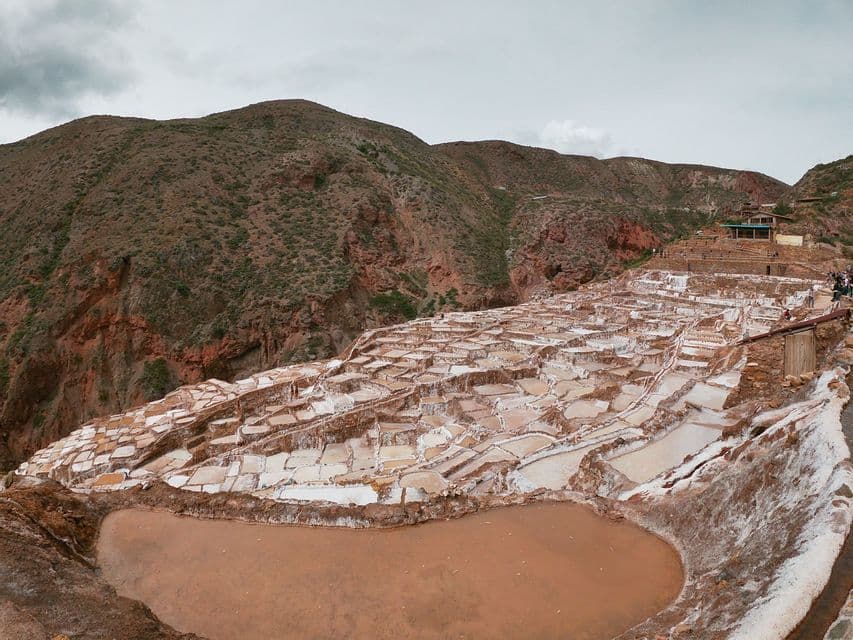 Un'ampia veduta di saline a terrazze bianche e marroni che ricoprono un versante montuoso sotto un cielo coperto.