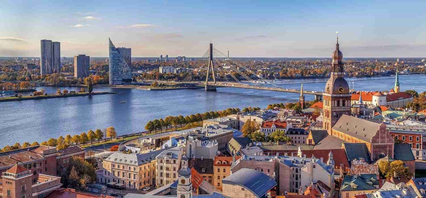 An aerial view of a city where a river and a large bridge separate historic buildings and a cathedral from modern skyscrapers.