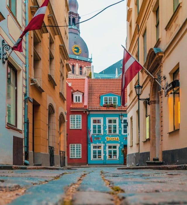 Une rue pavée étroite vue en contre-plongée, bordée de bâtiments colorés, avec une tour d'horloge visible en arrière-plan.