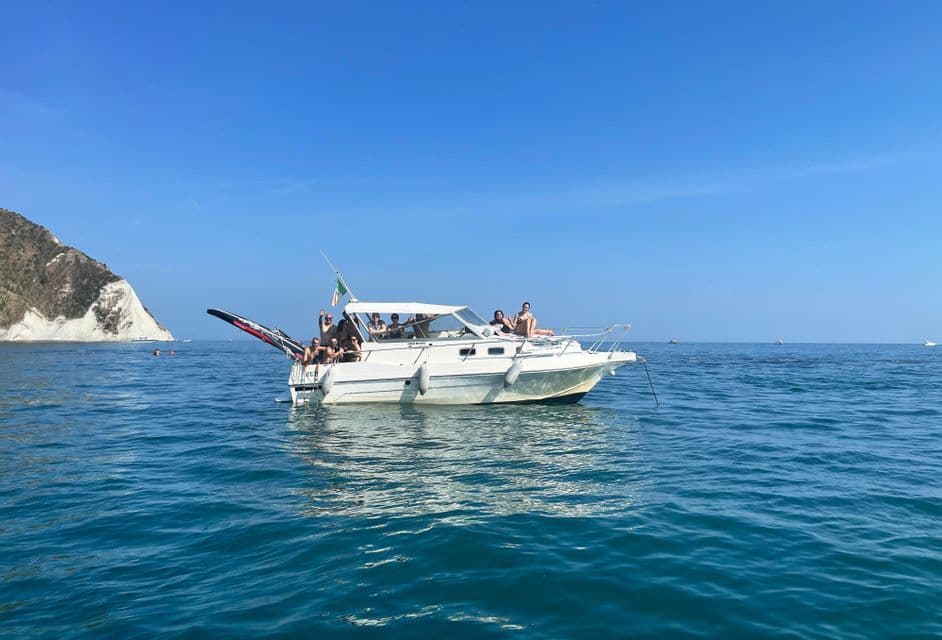 Un gruppo WeRoad in relax su un motoscafo bianco in mare aperto, con scogliera sullo sfondo.