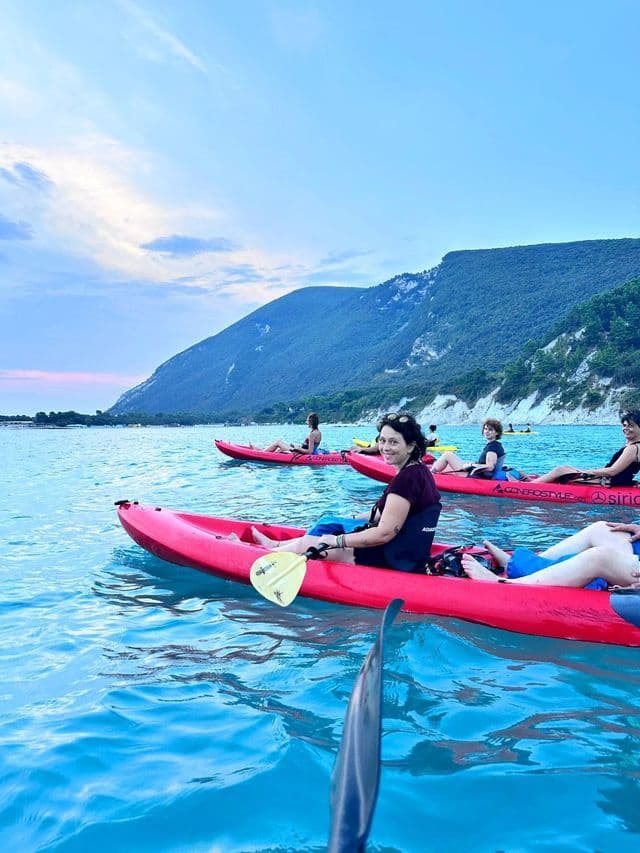 Un viaggio di gruppo WeRoad in kayak rossi su acqua turchese, con una costa montuosa verde sullo sfondo.