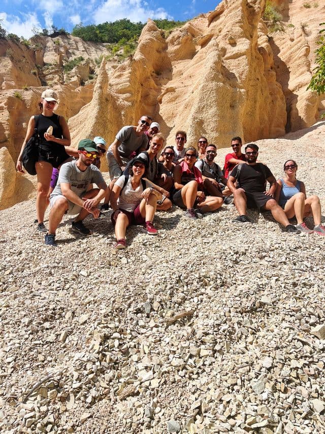 Un viaggio di gruppo WeRoad in posa per una foto su un pendio ghiaioso davanti a grandi formazioni rocciose erose in una giornata di sole.