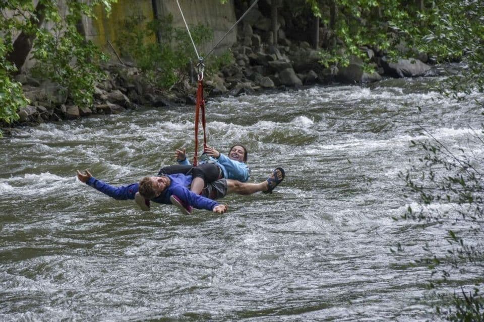 Dos viajeros de WeRoad sonriendo al cruzar un río caudaloso en tirolina.