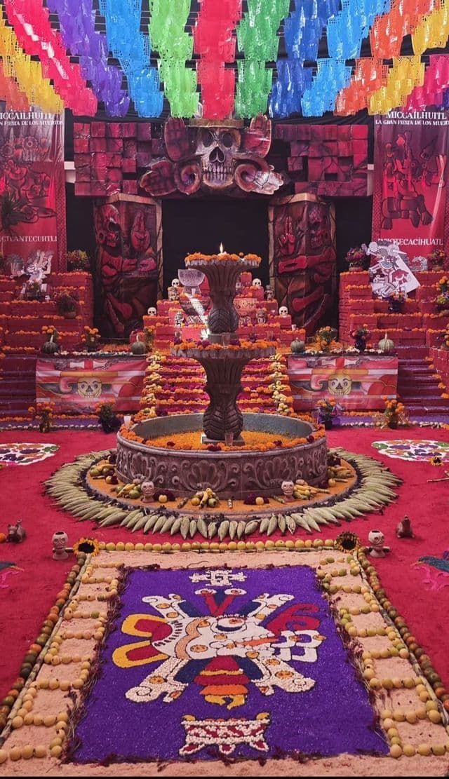 Un'elaborata ofrenda del Giorno dei Morti con una fontana centrale, calendule, teschi e colorati striscioni di papel picado.