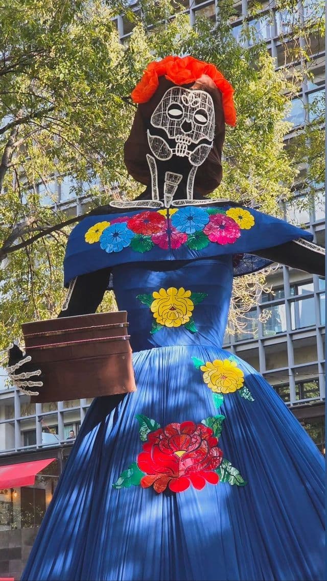 Una grande statua all'aperto di una figura di Calavera Catrina in un tradizionale abito blu adornato con motivi floreali colorati.