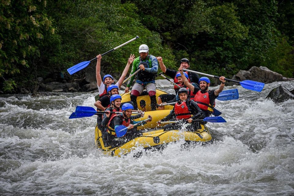 Un grupo de WeRoad celebra desde una balsa inflable amarilla mientras navega por rápidos de aguas bravas, con sus remos en alto.