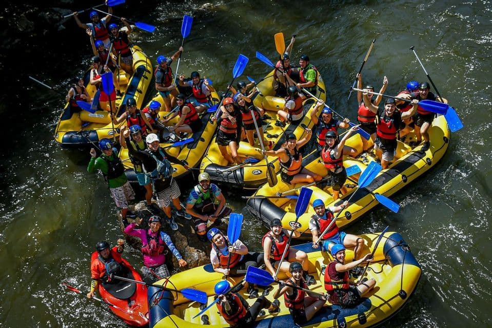 Una veduta aerea di un numeroso gruppo WeRoad che sorride su gommoni gialli in un fiume, con le pagaie alzate.