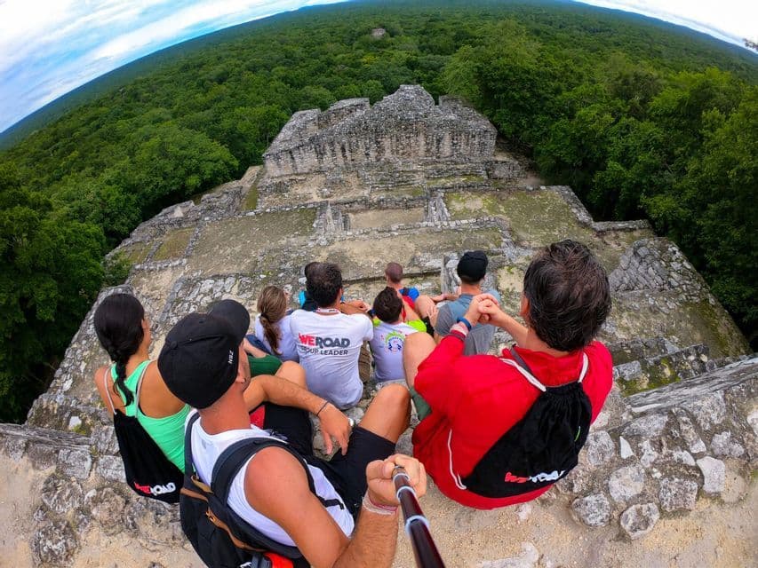 Un grupo de WeRoad se hace una selfie sentado sobre antiguas ruinas de piedra, con vistas a una vasta selva verde.