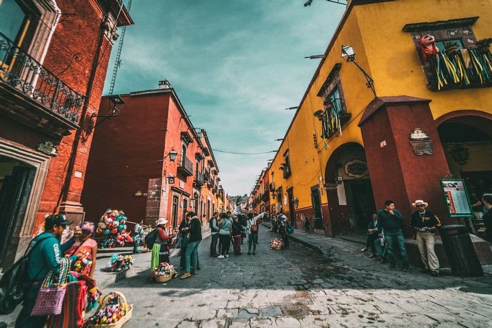 A low-angle view of a WeRoad group trip gathered on a cobblestone street between vibrant red and yellow buildings.