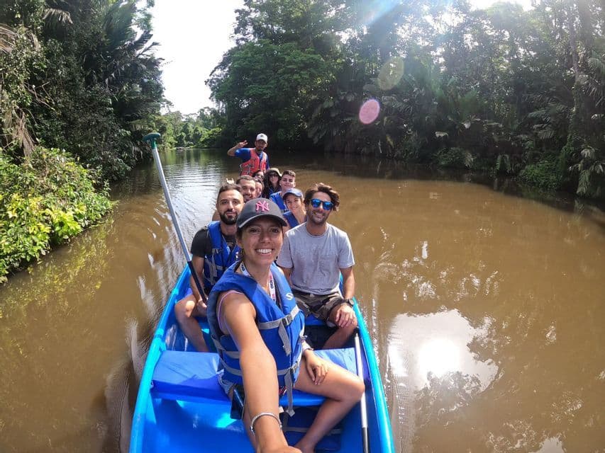 Une femme prend un selfie avec son groupe de voyage WeRoad, installée dans un canoë bleu sur une rivière au cœur d'une jungle luxuriante.