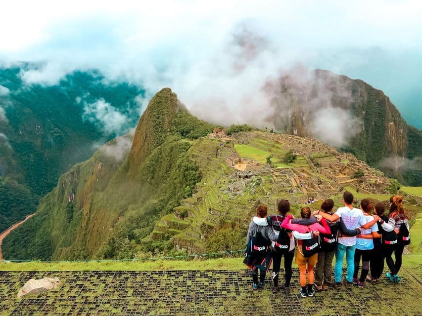 A WeRoad group trip with their arms around each other, looking out over ancient mountain ruins shrouded in clouds and mist.