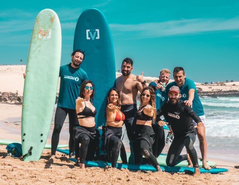 Eine WeRoad-Gruppenreise in Neoprenanzügen und Badebekleidung posiert gemeinsam für ein Foto mit Surfbrettern an einem sonnigen Sandstrand.