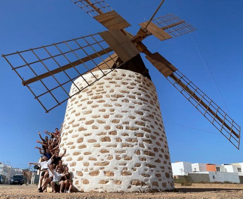 Eine WeRoad-Gruppe posiert am Fuße einer großen, traditionellen Steinwindmühle unter klarem blauem Himmel für ein Foto.